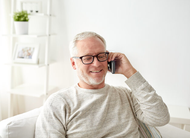 Adobe Stock | Syda Productions Männliche Person mittleren Alters sitzt auf dem Sofa und telefoniert. Sie hat einen freundlichen Gesichtsausdruck.