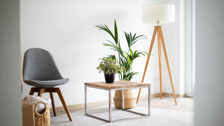 Helle, modern eingerichtete Wohnunung der WBG Lünen mit einem grauen Stuhl, kleinem Holztisch, Zimmerpflanzen und einer Stehlampe. Der Raum wirkt ruhig und freundlich, mit viel Tageslicht durch ein Fenster.