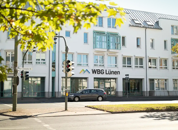 Straßenansicht eines weißen Bürogebäudes mit dem Schriftzug „WBG Lünen“. Vor dem Gebäude verläuft eine Straße, im Vordergrund sind Bäume zu sehen.